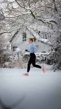 Hardlopend door de sneeuw, langs een wit huis onder besneeuwde takken.