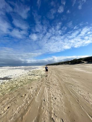 Hardlopend over een breed strand onder een hoge lucht met wolkenslierten.